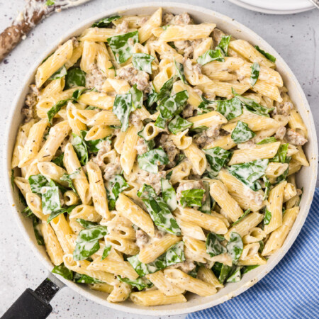 Creamy sausage pasta in a cream sauce mixed with spinach in a large skillet from above on a counter.