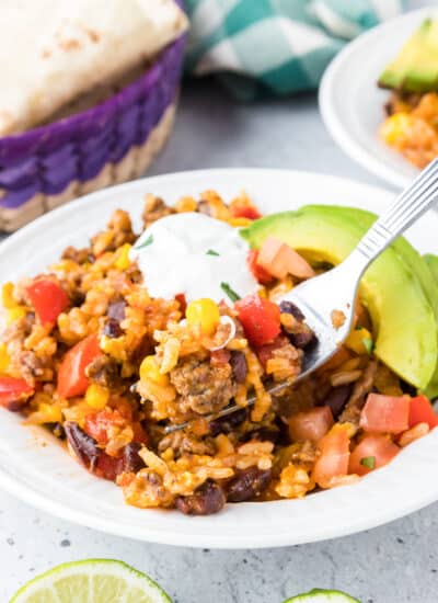 Ground beef burrito bowl full of toppings being scooped with a fork from the side.