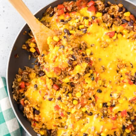 One pot burrito bowl covered in melty cheese being scooped from a pan with a wooden spoon from overhead.