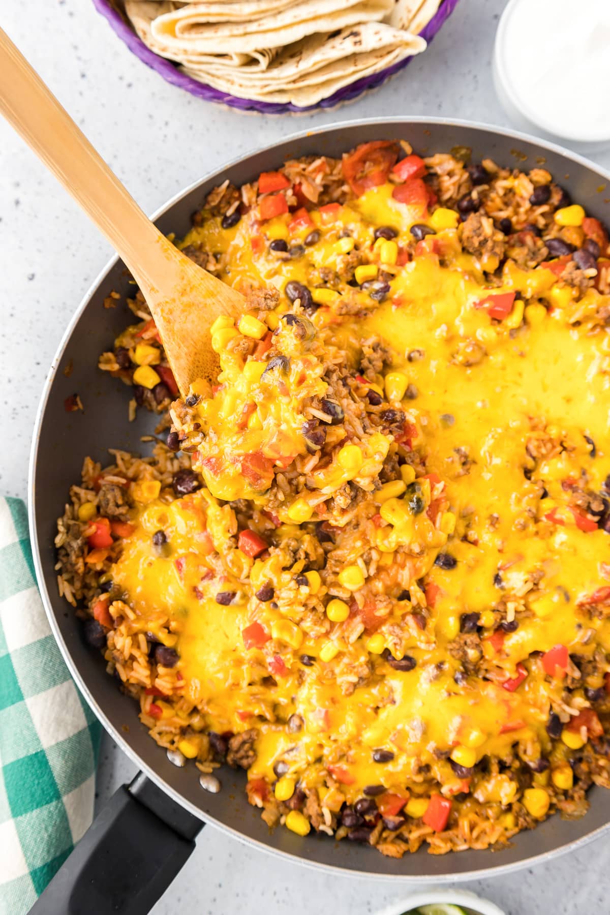 One pot burrito bowl covered in melty cheese being scooped from a pan with a wooden spoon from overhead.