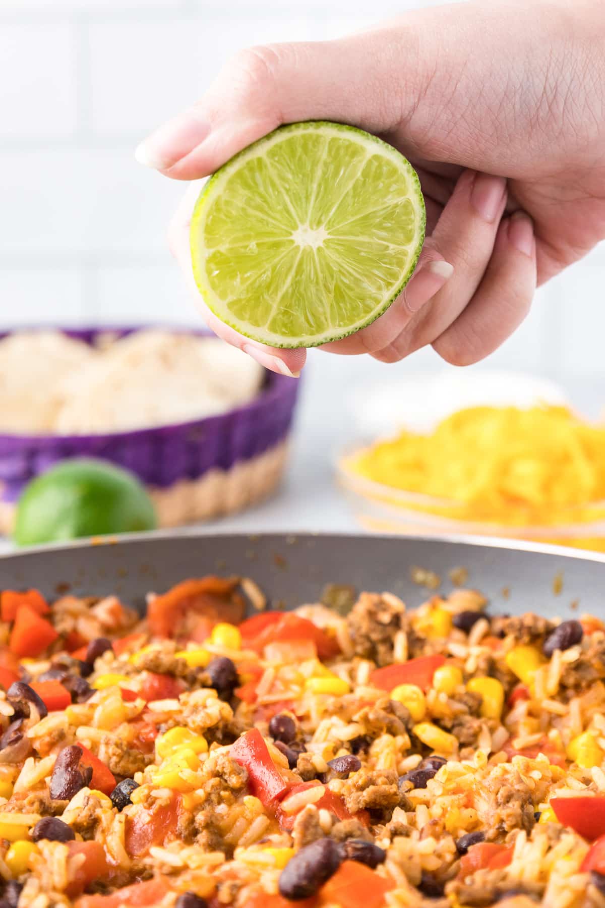 Lime juice being squeezed by a hand from the side over the burrito bowl mixed rice.