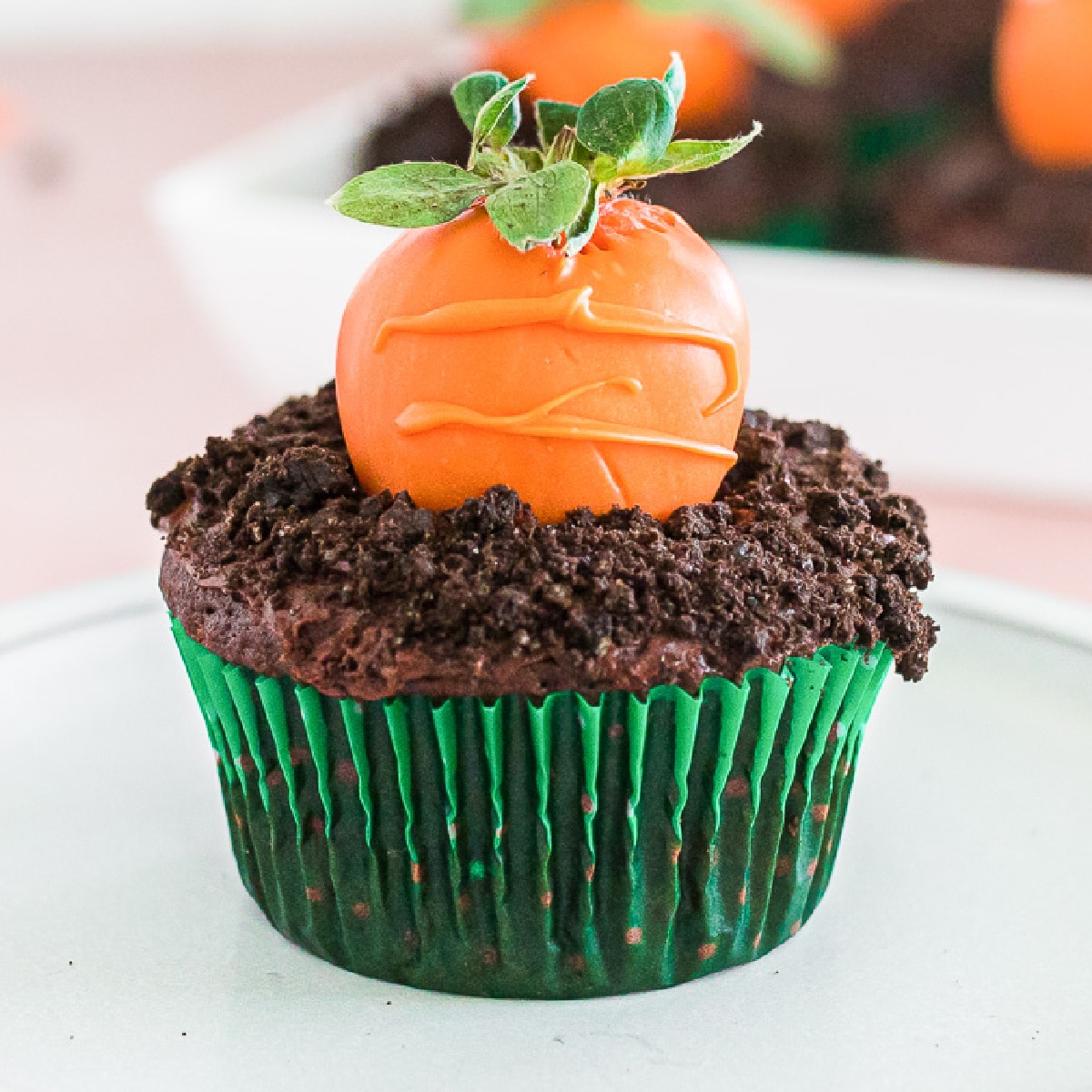 Close up of a cupcake with an orange chocolate covered strawberry decorated to look like a carrot in chocolate cookie crumble dirt.