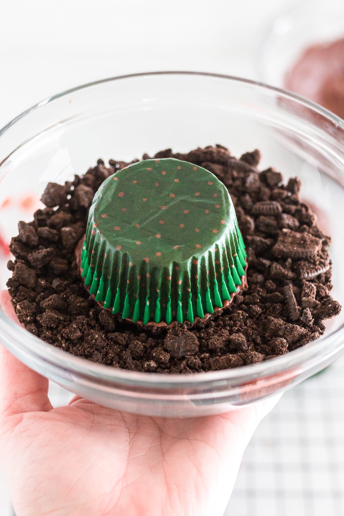 A chocolate cupcake upside down in a bowl of chocolate cookie crumbs.
