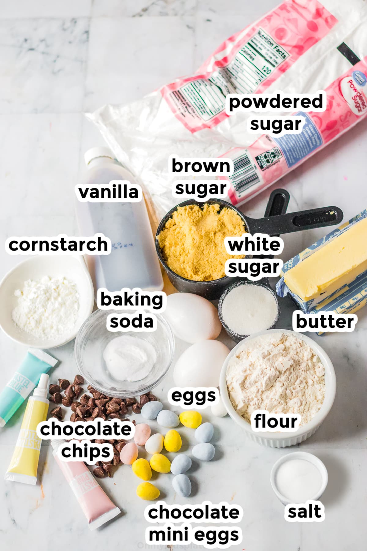 Ingredients for Easter egg cookie cake on a counter in bowls with text labels.