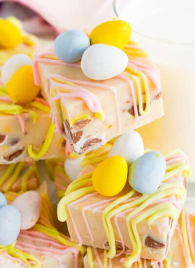 A stack of white chocolate Easter Fudge from the side decorated with chocolate mini eggs.