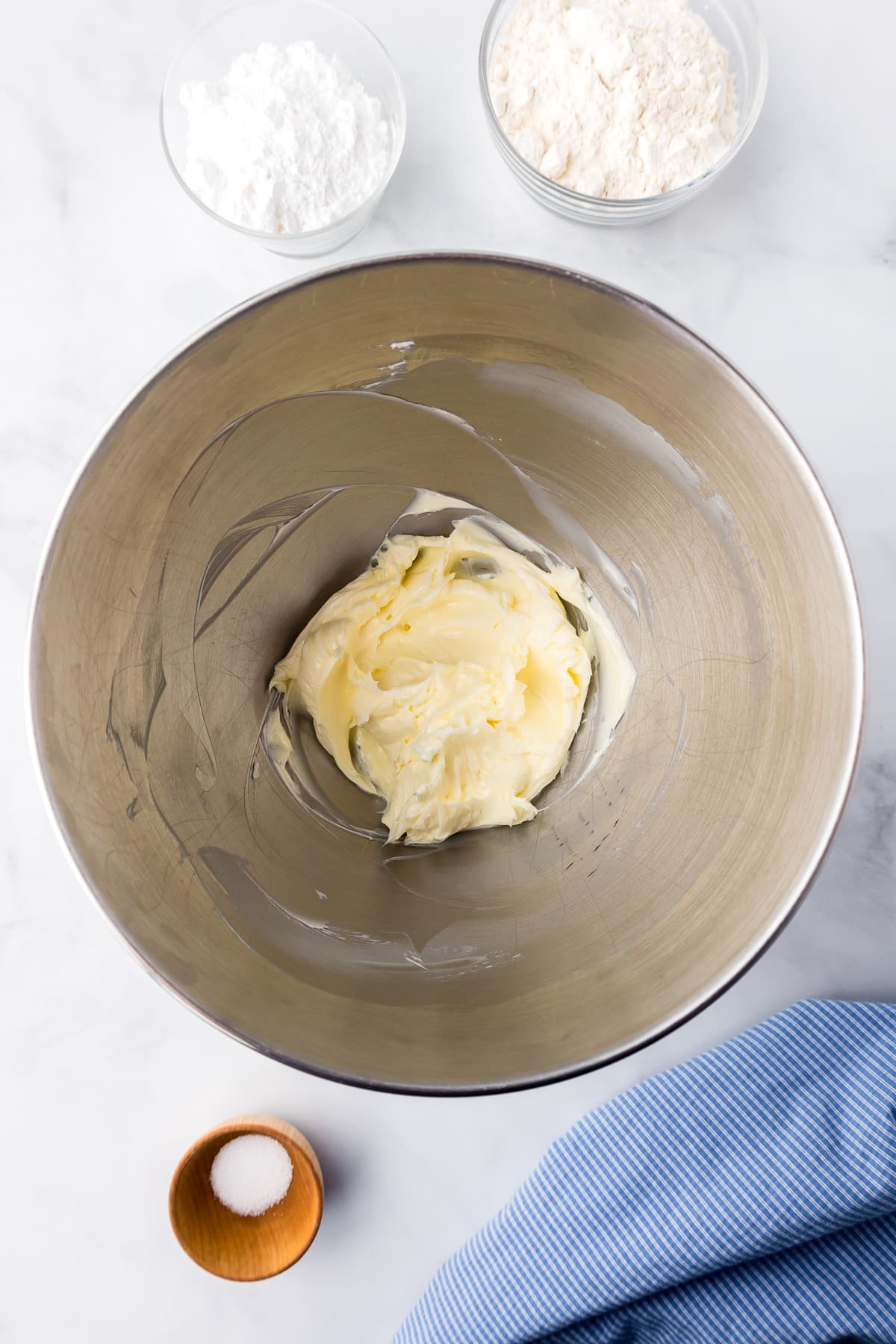Butter and sugar creamed together in a mixing bowl with more dry ingredients in bowls on the counter nearby.