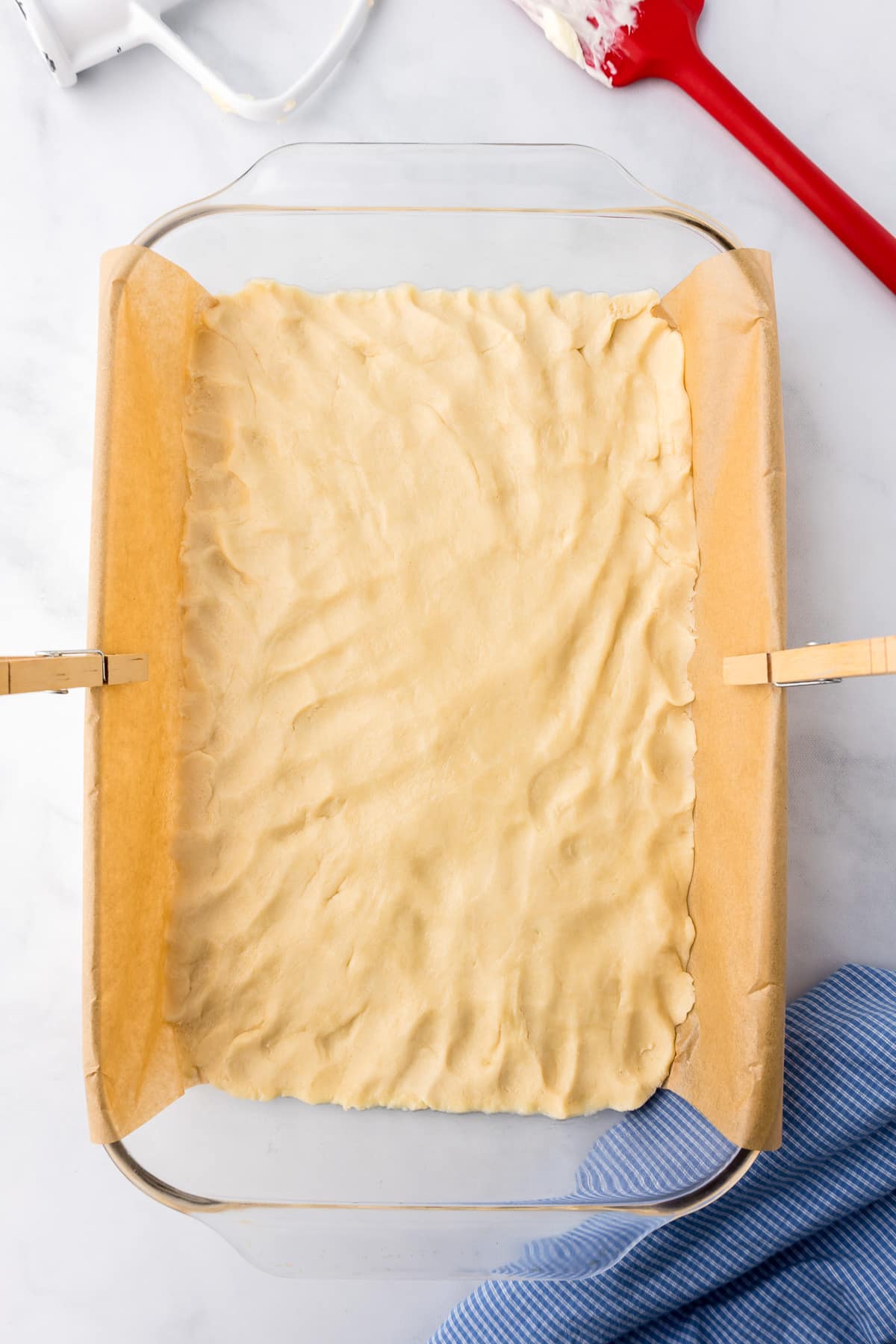 Dough for the crust pressed into a parchment lined glass baking dish. Clothespins hold the parchment paper steady.