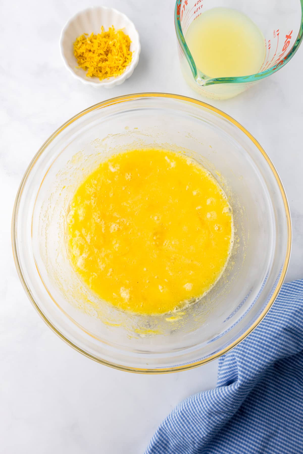 Lemon juice and lemon zest being added to a large bowl of lemon curd filling.