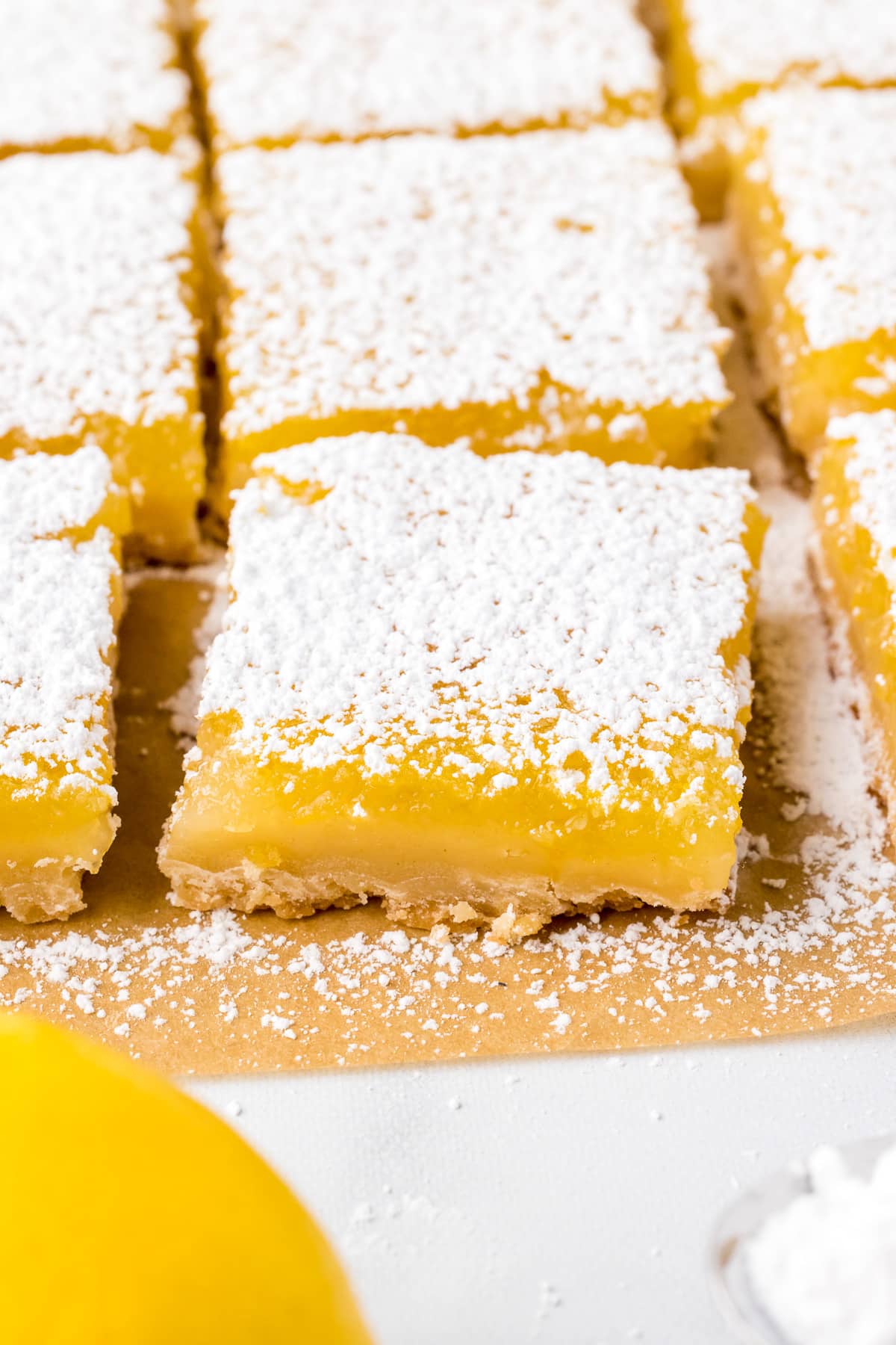A single lemon bar pulled away from the rest of the lemon bars in rows on from the side.
