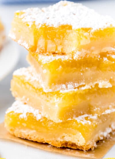 Tall stack of lemon bars covered in powdered sugar with the top lemon bar missing a bite.
