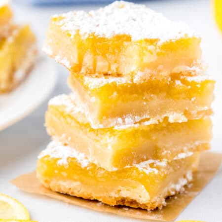Tall stack of lemon bars covered in powdered sugar with the top lemon bar missing a bite.