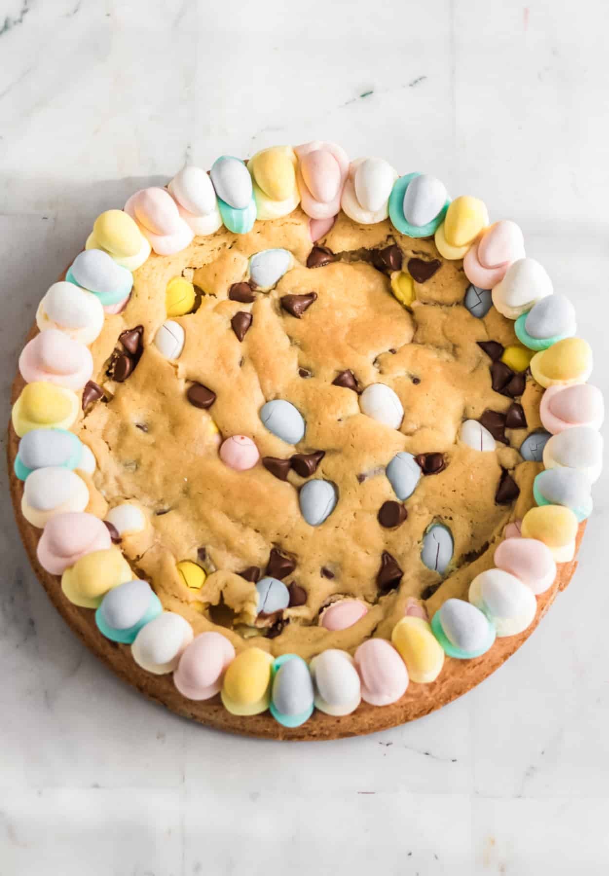 Chocolate mini egg cookie cake decorated with frosting and colored chocolate eggs around the edge for Easter.