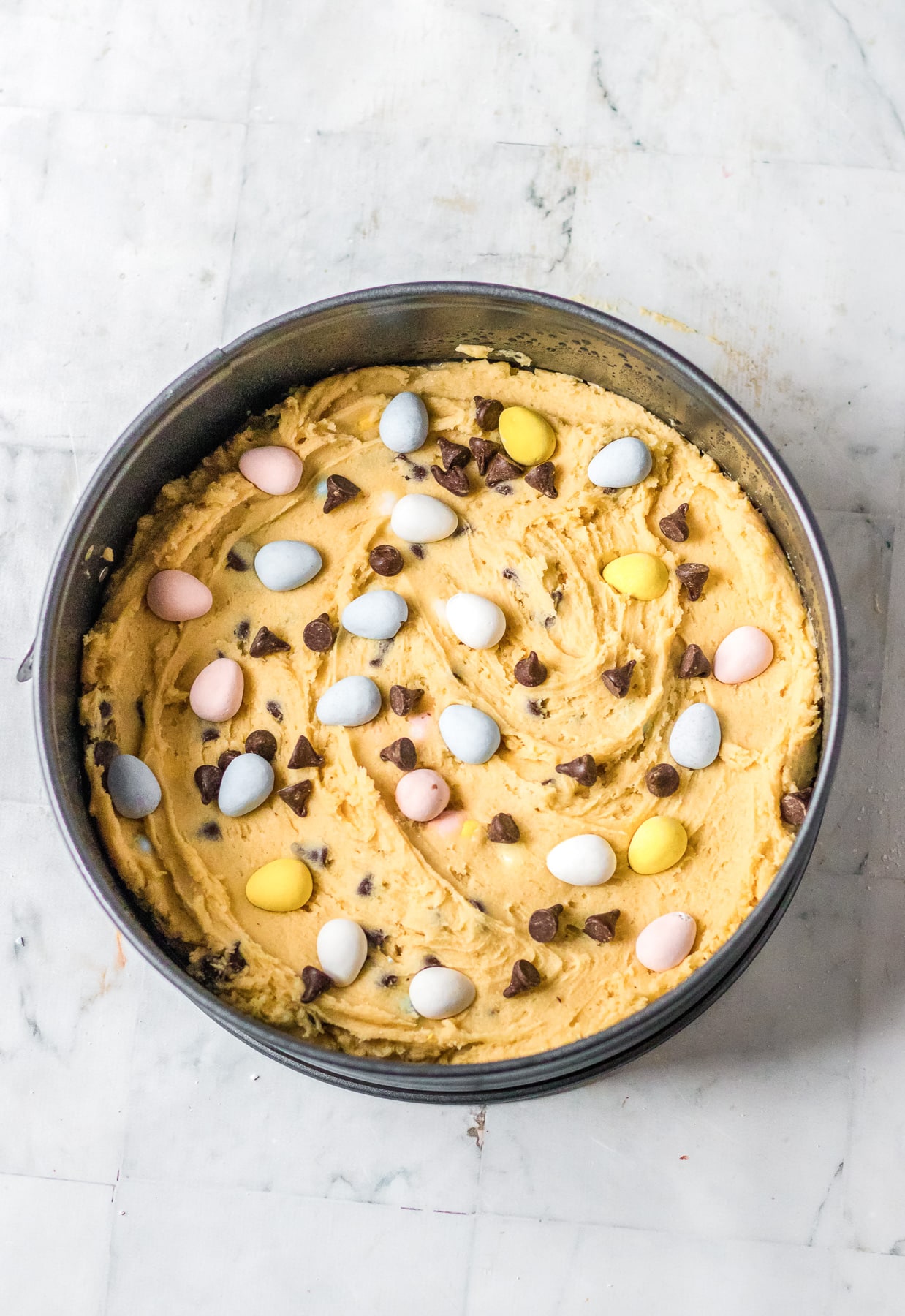 Cookie dough in a springform pan topped with more mini chocolate eggs.