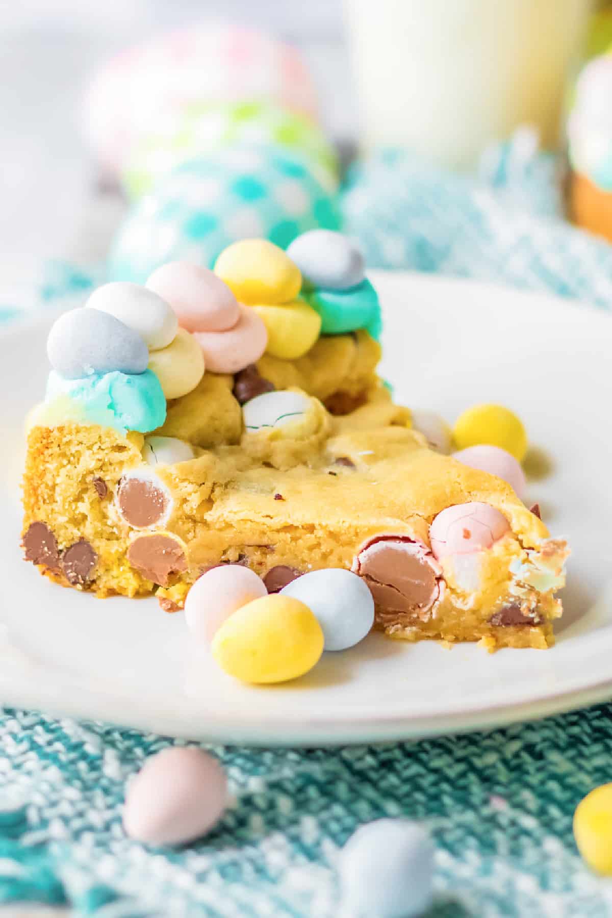 A slice of chocolate mini egg easter cookie cake on a plate from the side topped with more candy eggs from the side.