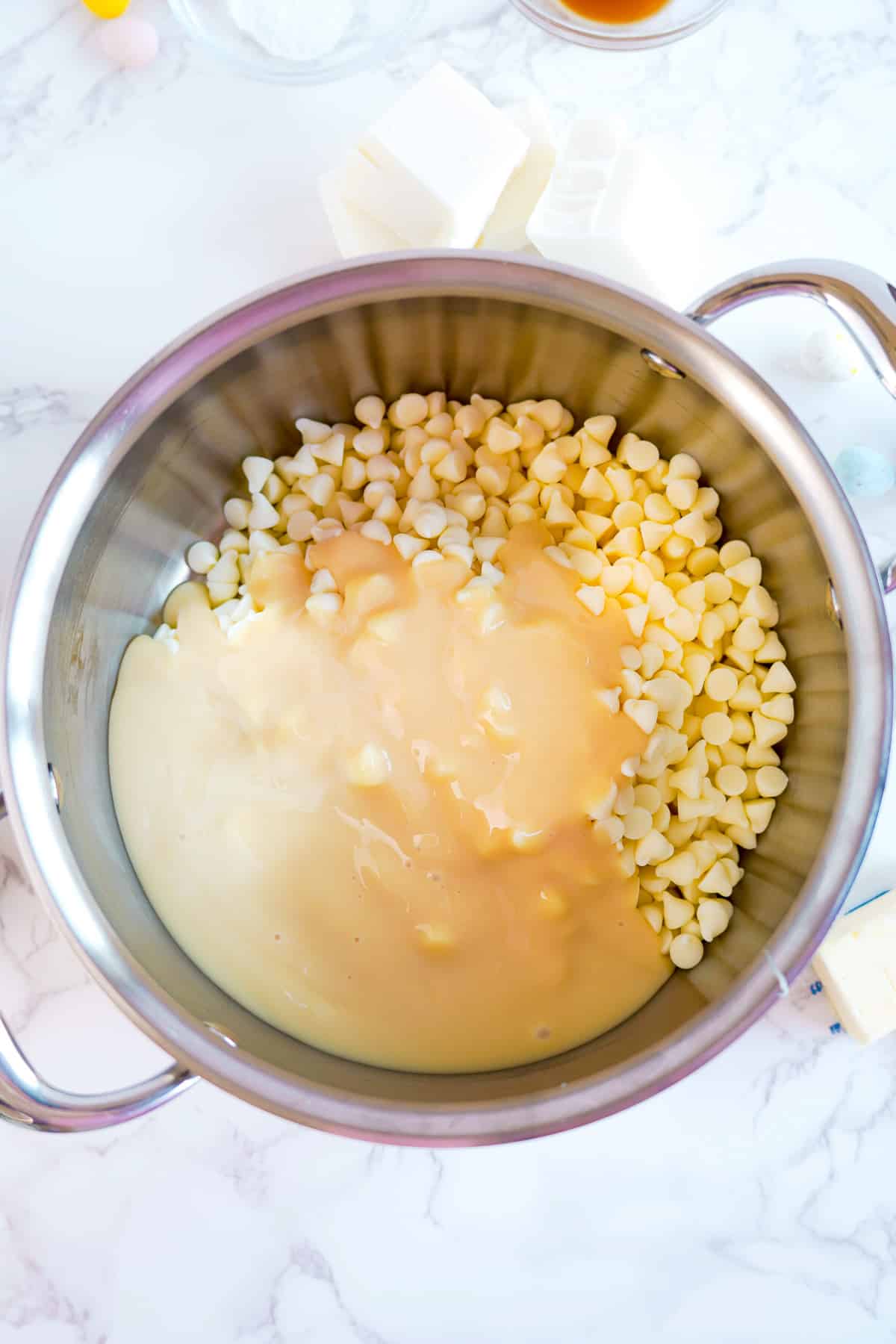 Sweetened condensed milk and white chocolate chips in a pan from above.