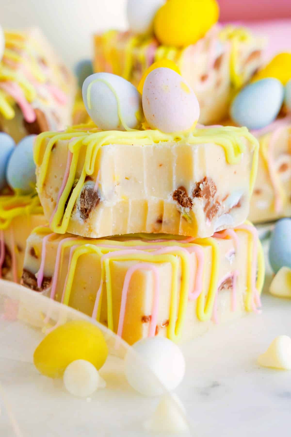 Two pieces of stacked white chocolate Easter fudge full of chocolate mini eggs with a bite missing on the top piece.