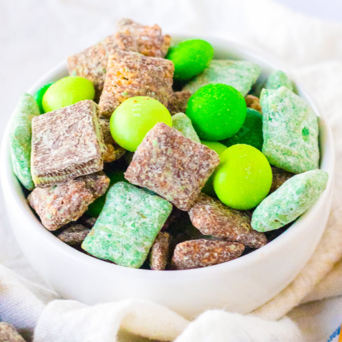 Close up view of green and brown mint chocolate muddy buddies in a snack bowl.