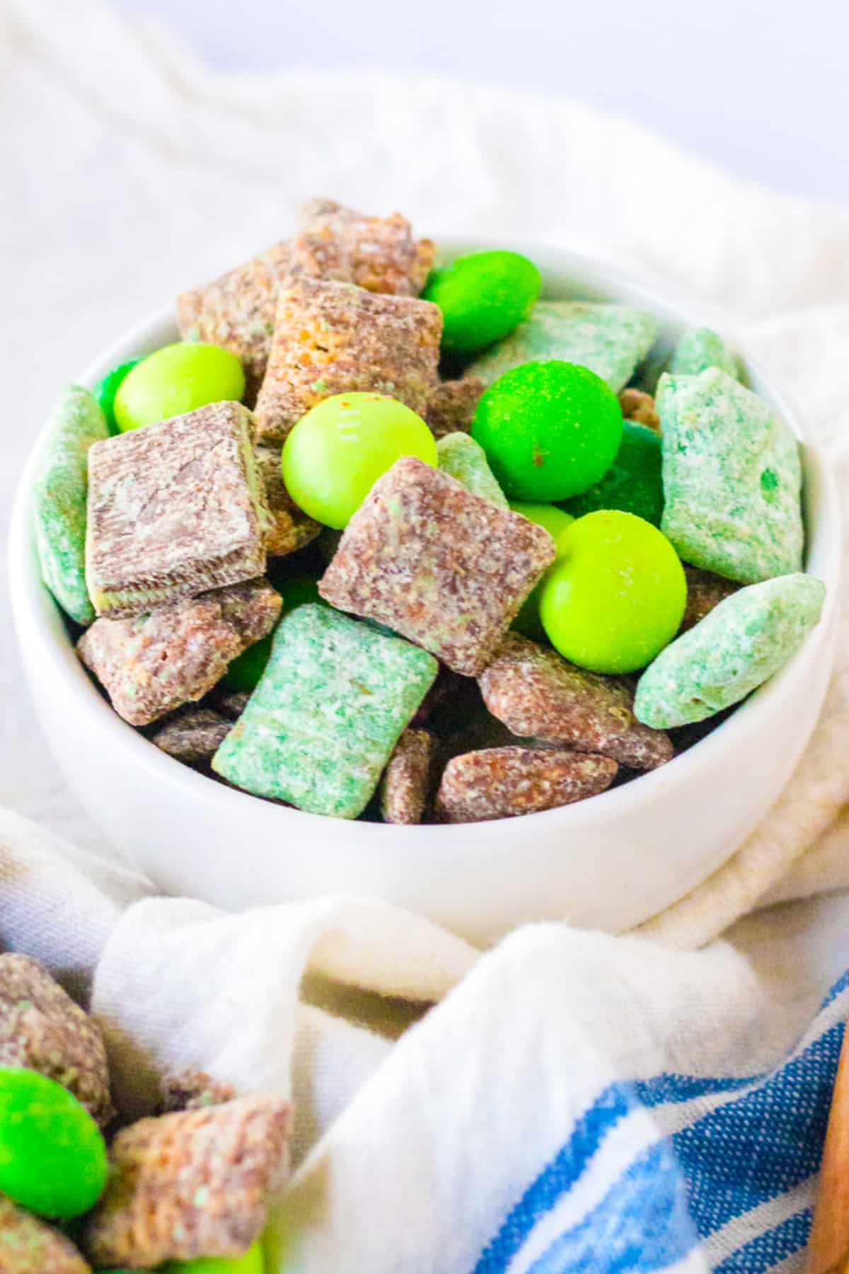 Mint muddy buddies with brown and green covered chex in a snack bowl from the side.