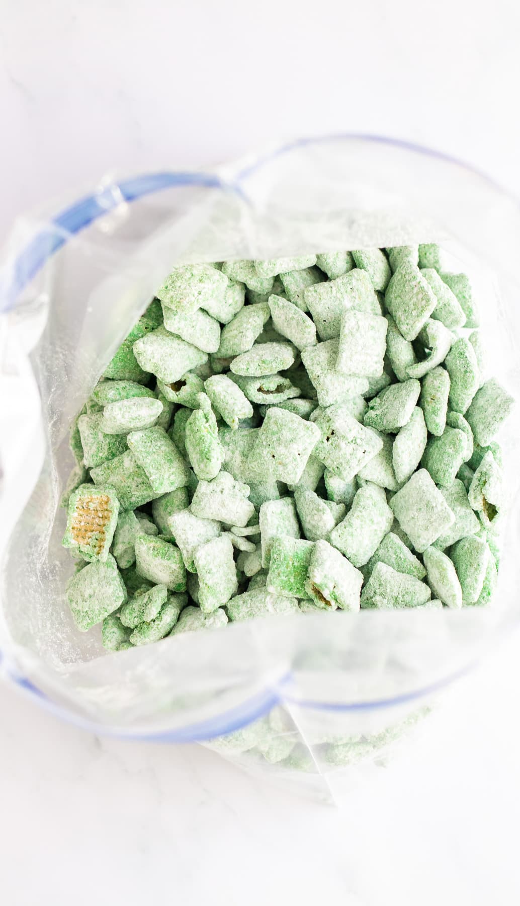 Rice chex cereal coated in green chocolate candy melts and powdered sugar in a large zip-top bag from overhead.