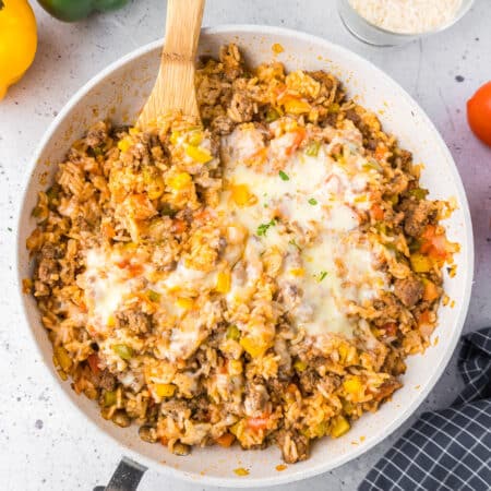 Square view of a deconstructed stuffed pepper rice and cheese dish in a large skillet from overhead being stirred with a wooden spoon.
