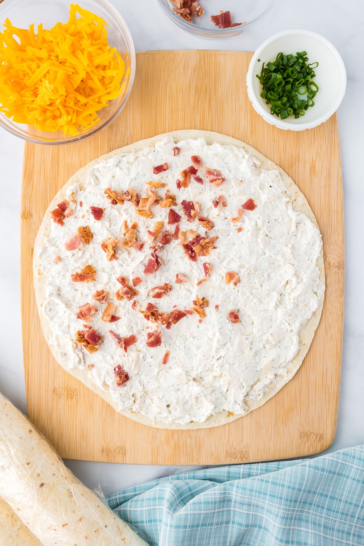 Sprinkling bacon on a tortilla covered in a cream cheese mixture from overhead.