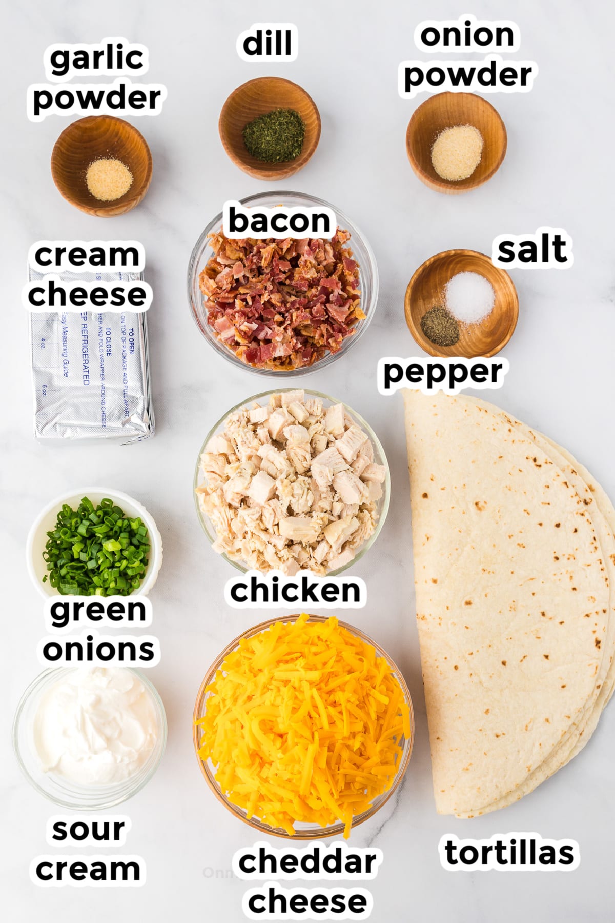 Ingredients for chicken bacon ranch pinwheels in bowls from overhead on a counter with text labels.