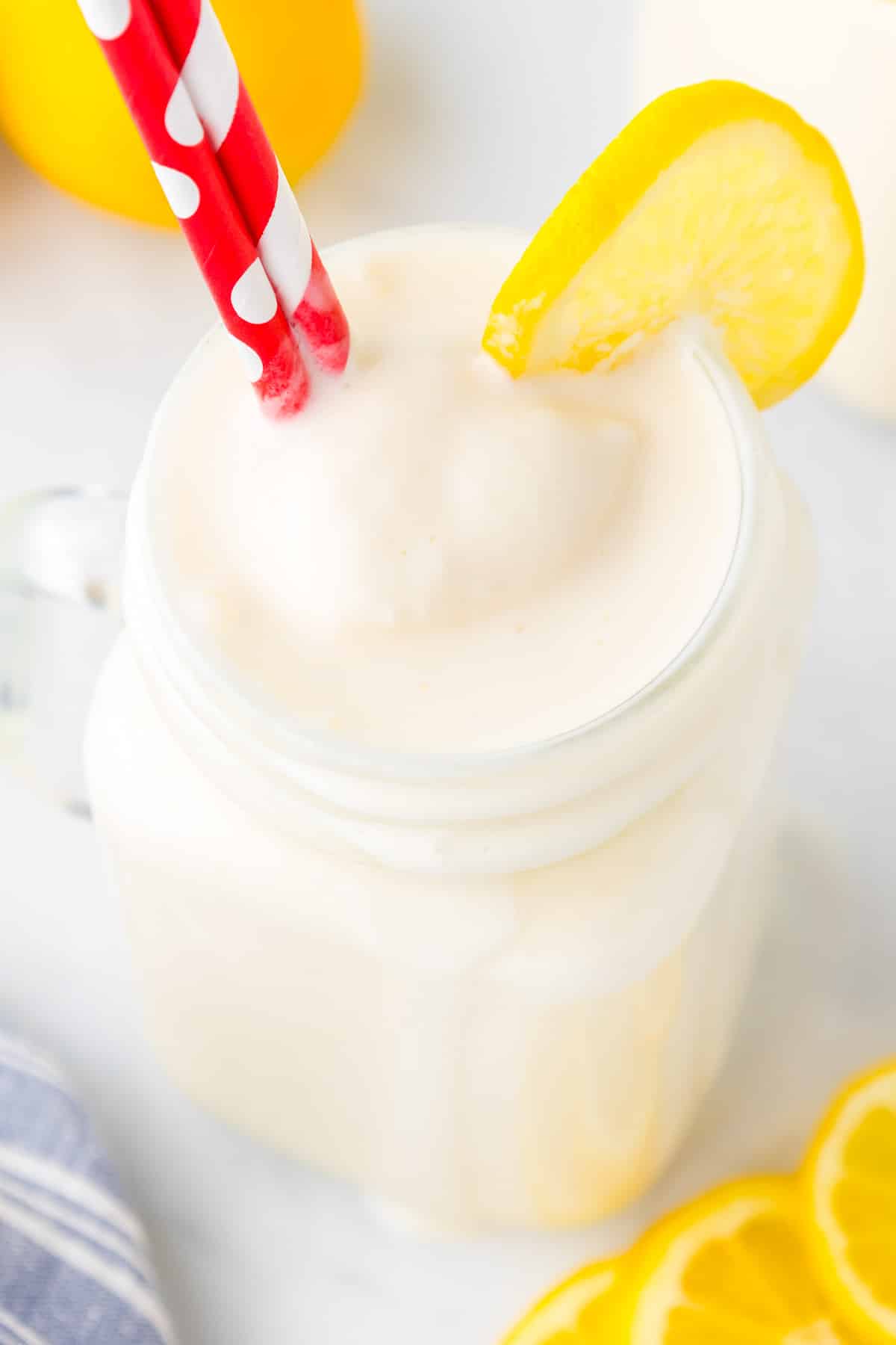 A frosted lemonade in a large glass from overhead with red straws and a lemon slice on the glass.
