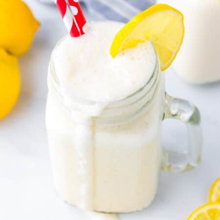 Close up overhead view of a frosted lemonade with a lemon slice and red straws with a big dribble down the side of the glass.