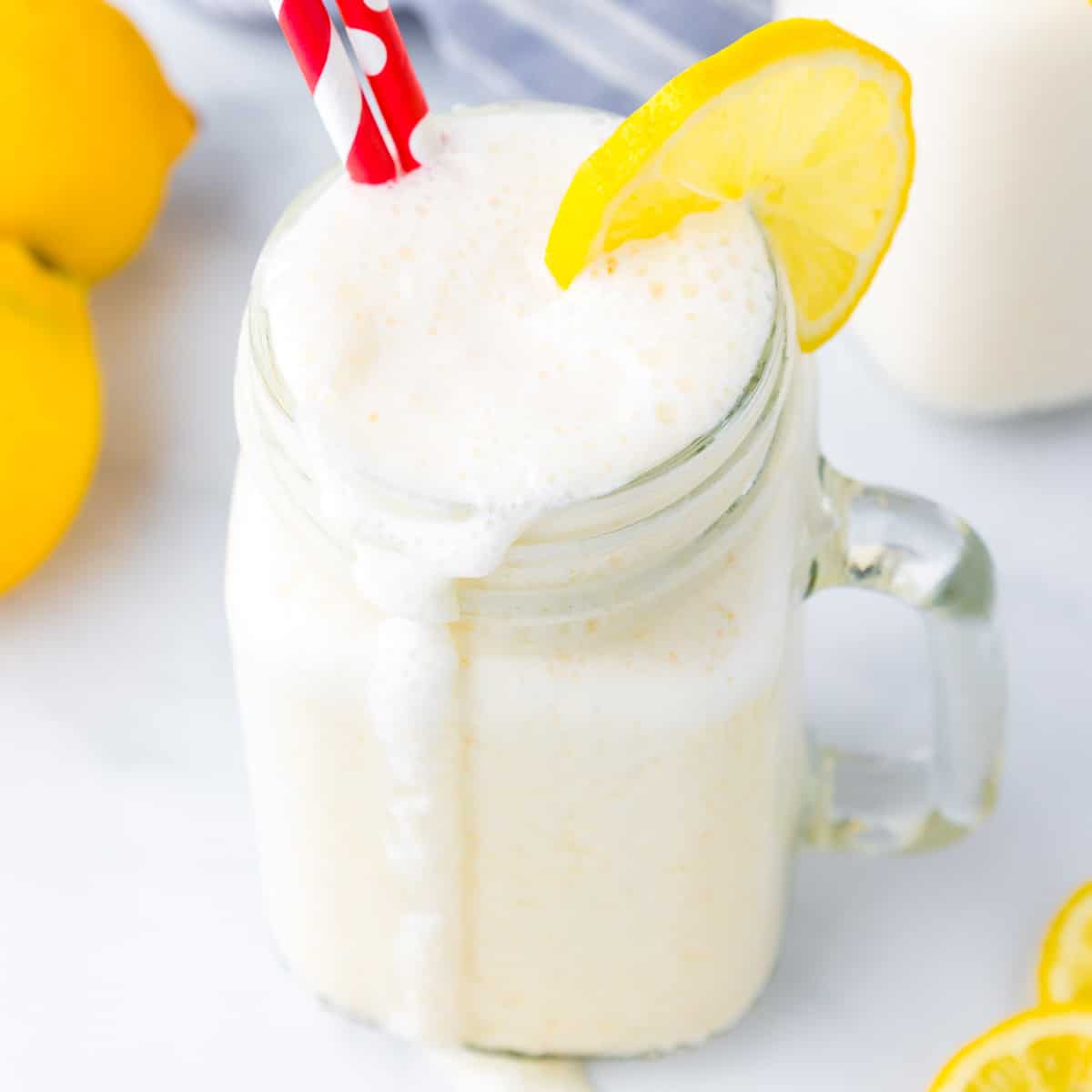 Close up overhead view of a frosted lemonade with a lemon slice and red straws with a big dribble down the side of the glass.