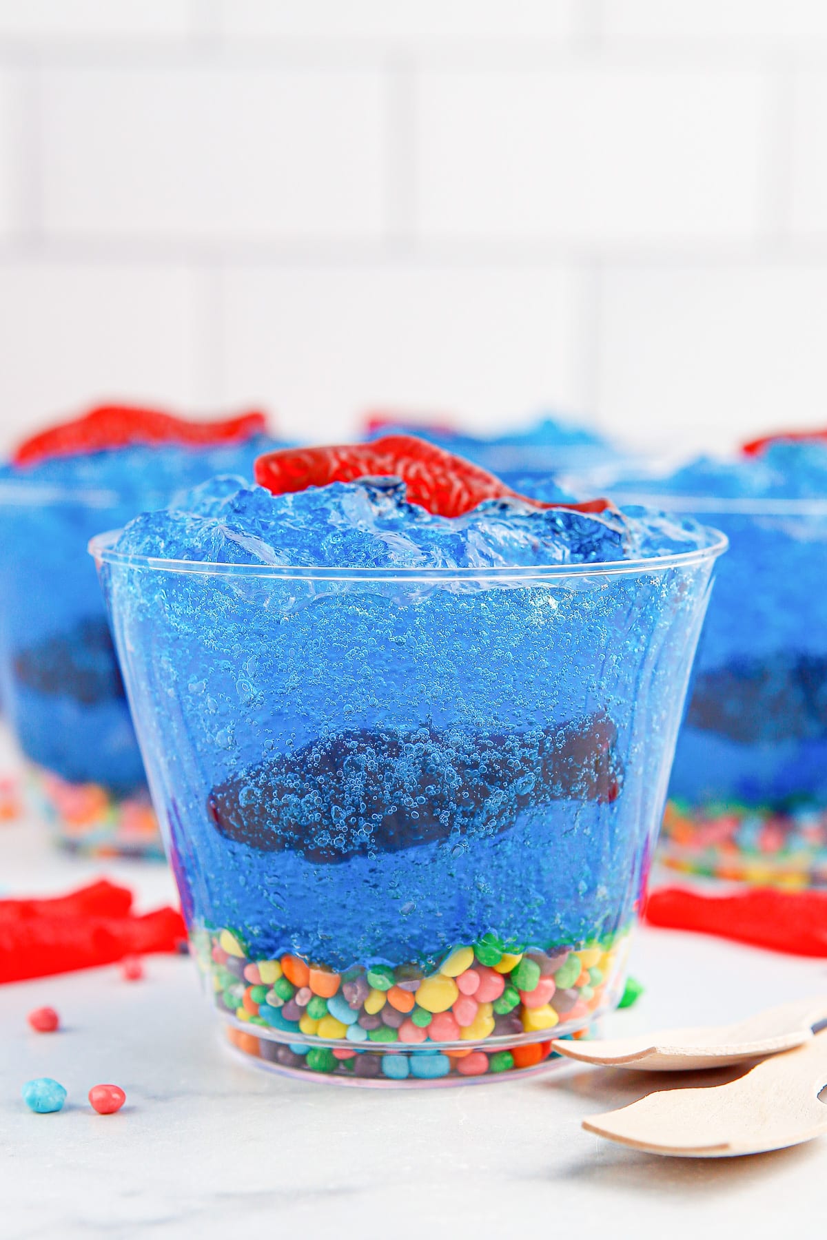 Side vie of bubbly blue gelatin with a candy fish inside and on top in a cup and colorful candy nerds on the bottom of the cup from the side.