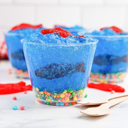 Side view of cups filled with blue jell-o, candy fish and candy rocks decorated to look like a fish tank.