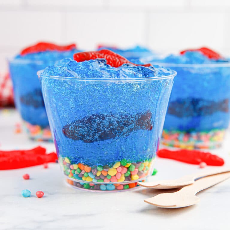 Side view of cups filled with blue jell-o, candy fish and candy rocks decorated to look like a fish tank.