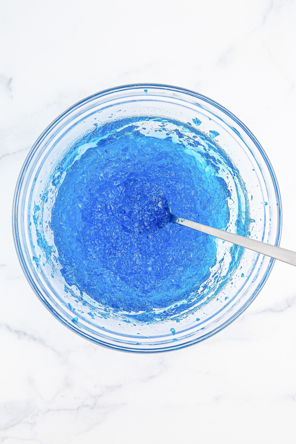Stirring blue gelatin in a bowl from overhead to make bubbles.