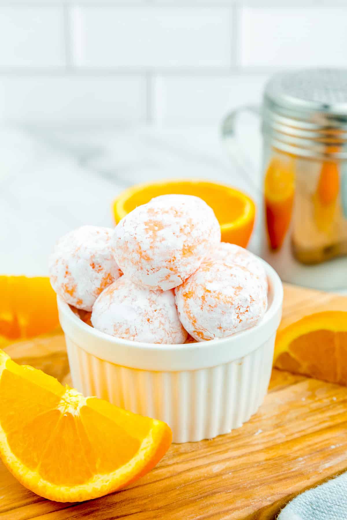 Creamsicle truffles covered in powdered sugar piled high in a bowl with slices of orange near the bowl on a cutting board.