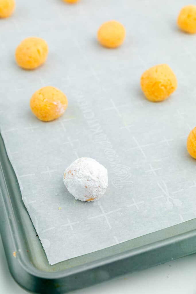Single orange creamsicle truffle focus on pan rolled in powdered sugar while the rest are orange on the pan without sugar coating.