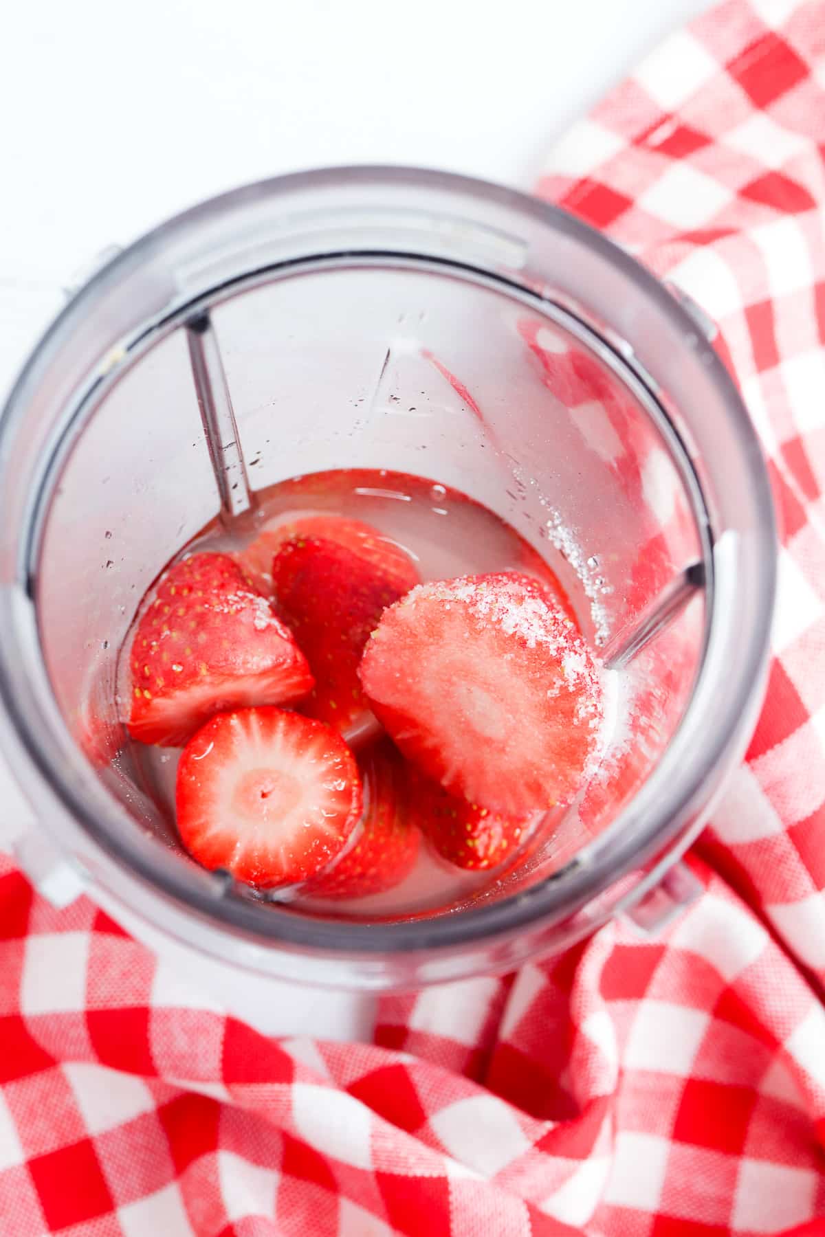 Strawberries, sugar and water in a blender from above.