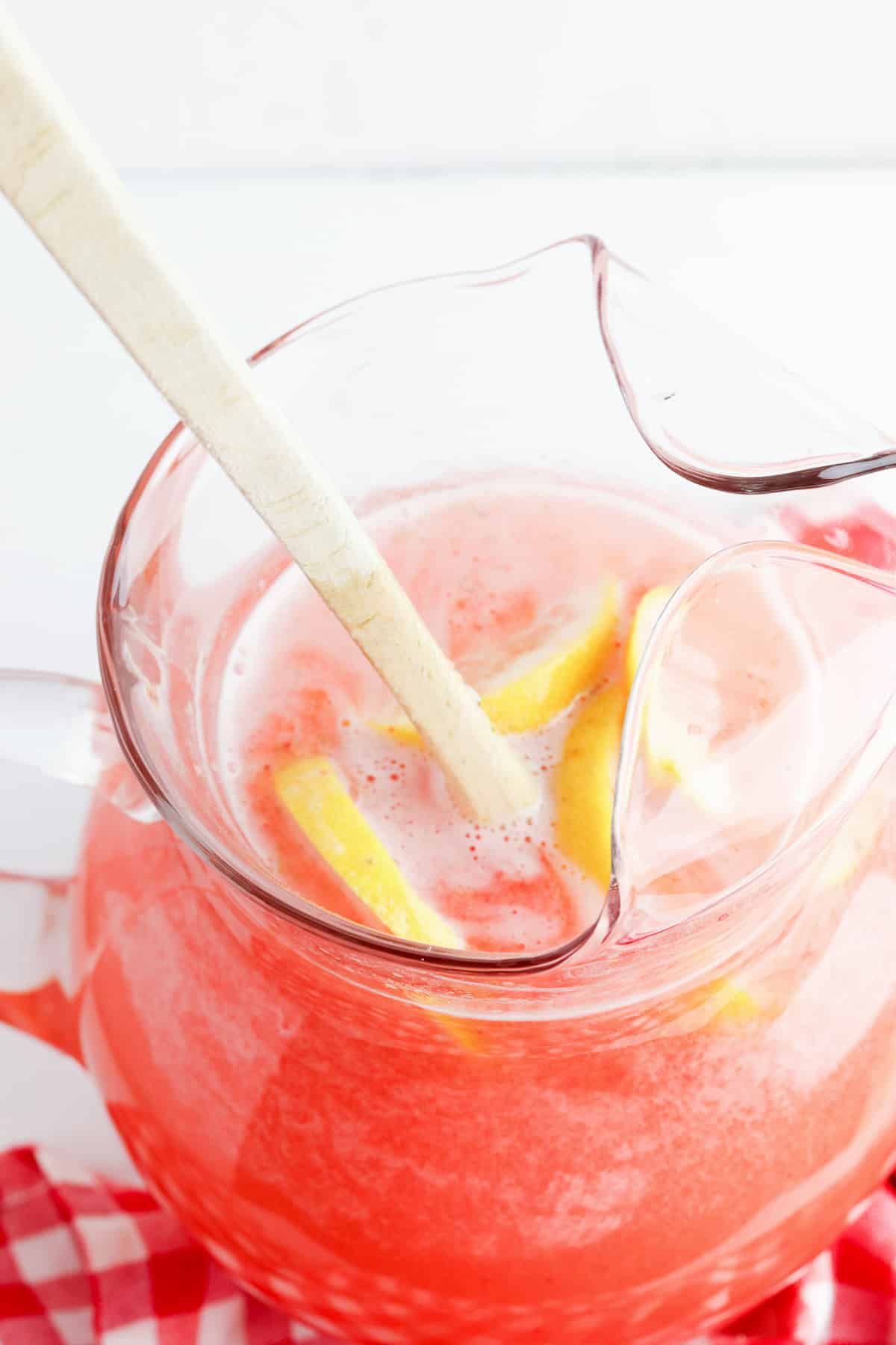 Strawberry lemonade in a pitcher form above being mixed with a wooden spoon.