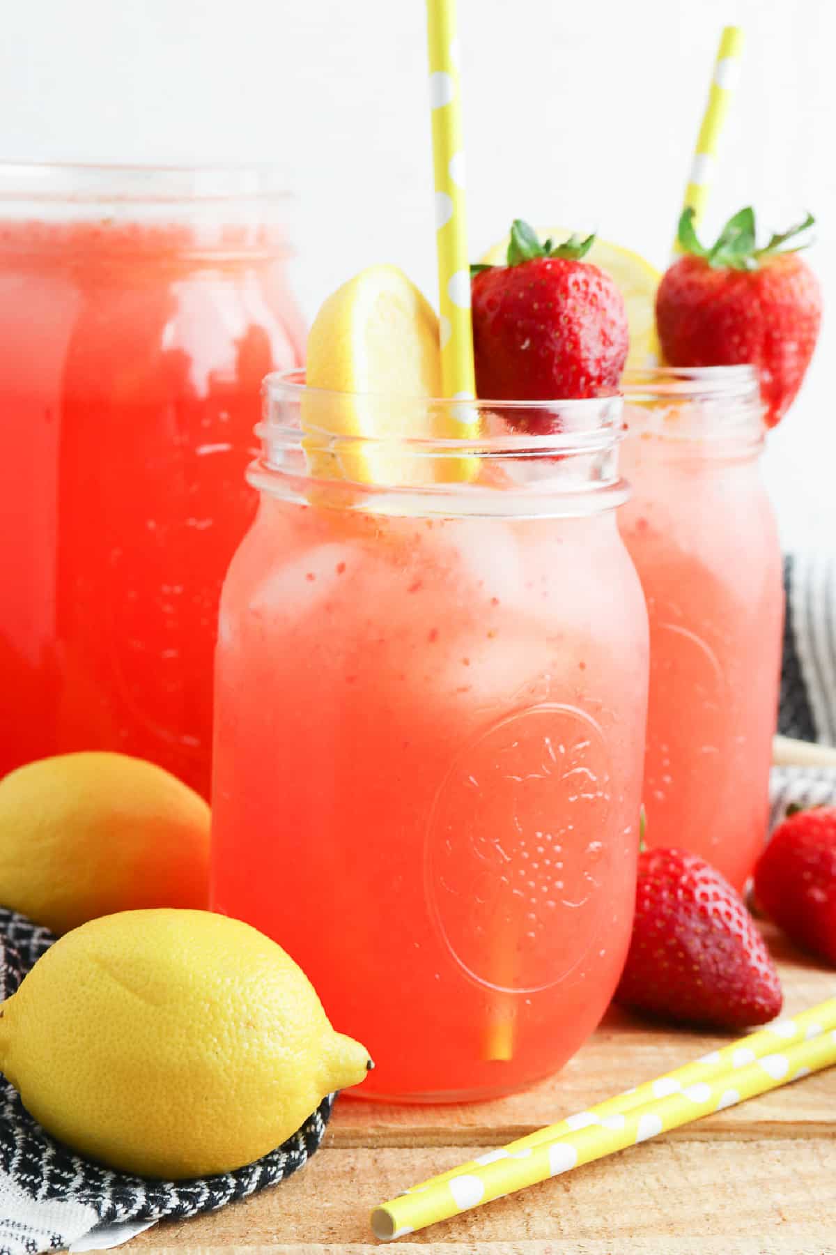 Strawberry lemonade in mason jar glasses from the side with more strawberries and lemon slices on top.