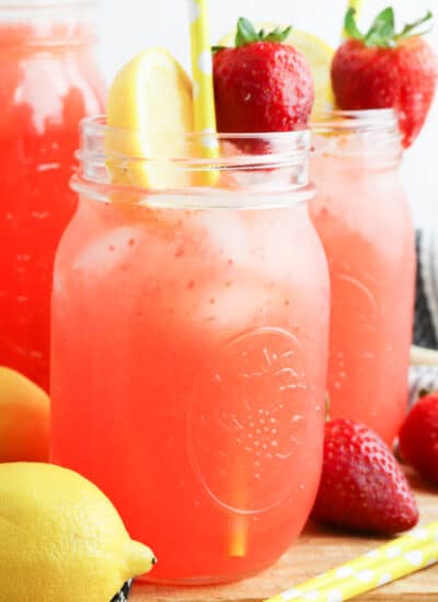 Side view of three glasses of strawberry lemonade topped with fresh fruit.
