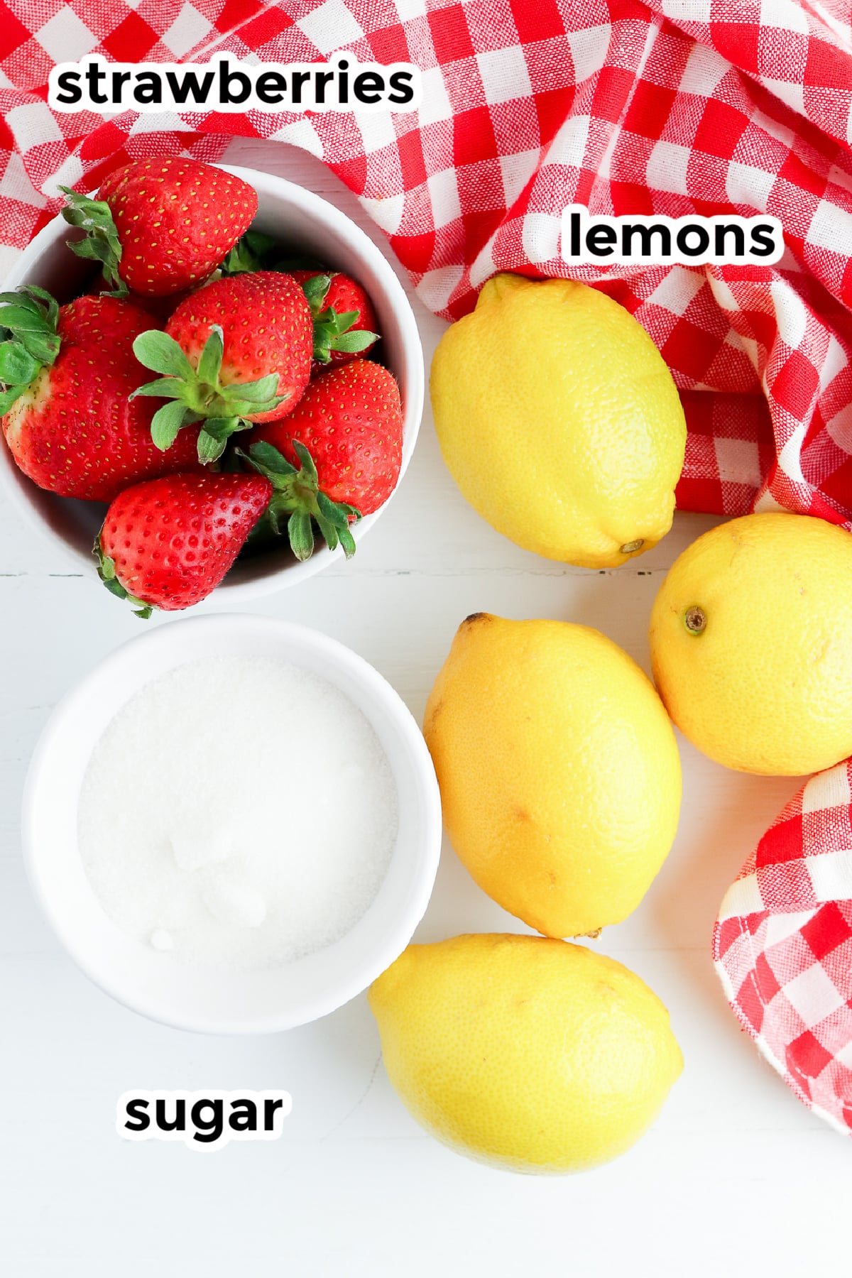 Strawberries, sugar and lemons in bowls on a counter with a towel from overhead with title text overlay.