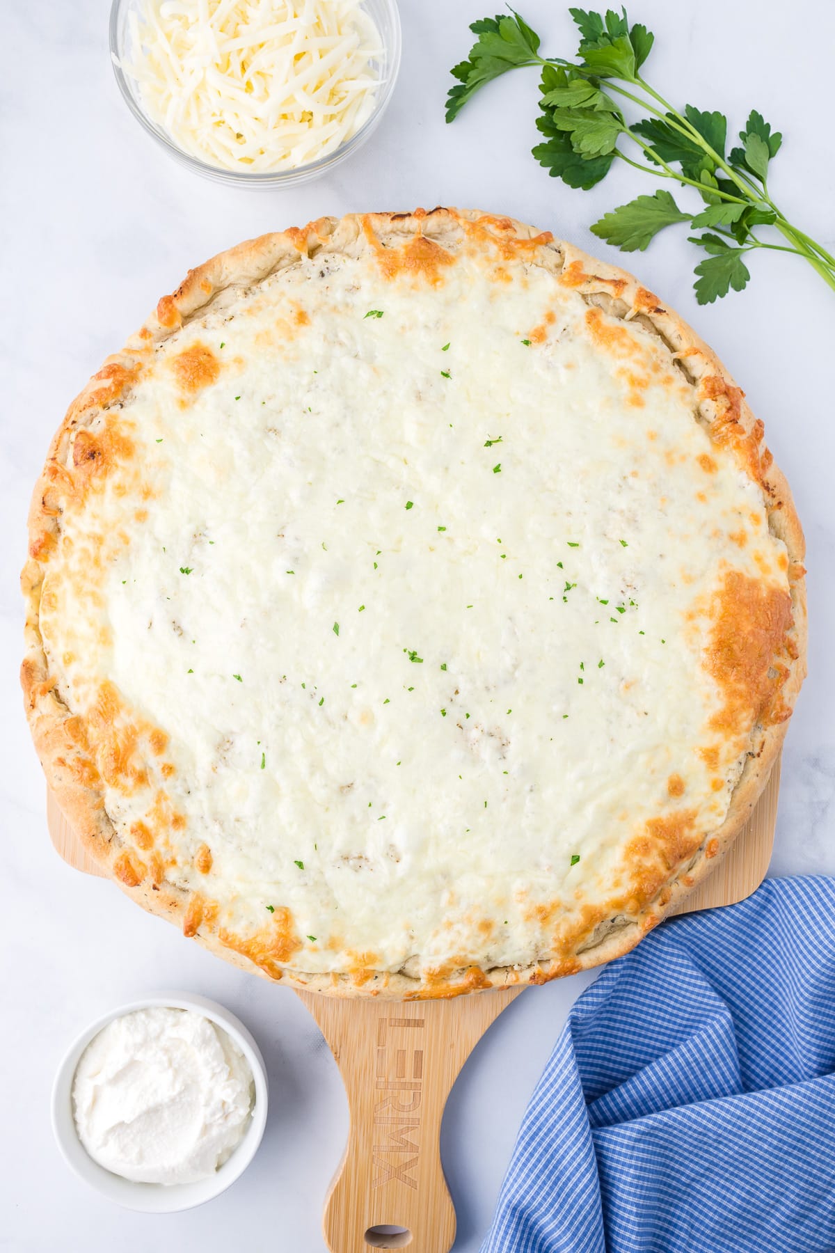 Baked pizza covered in white cheese on a wooden pizza paddle.