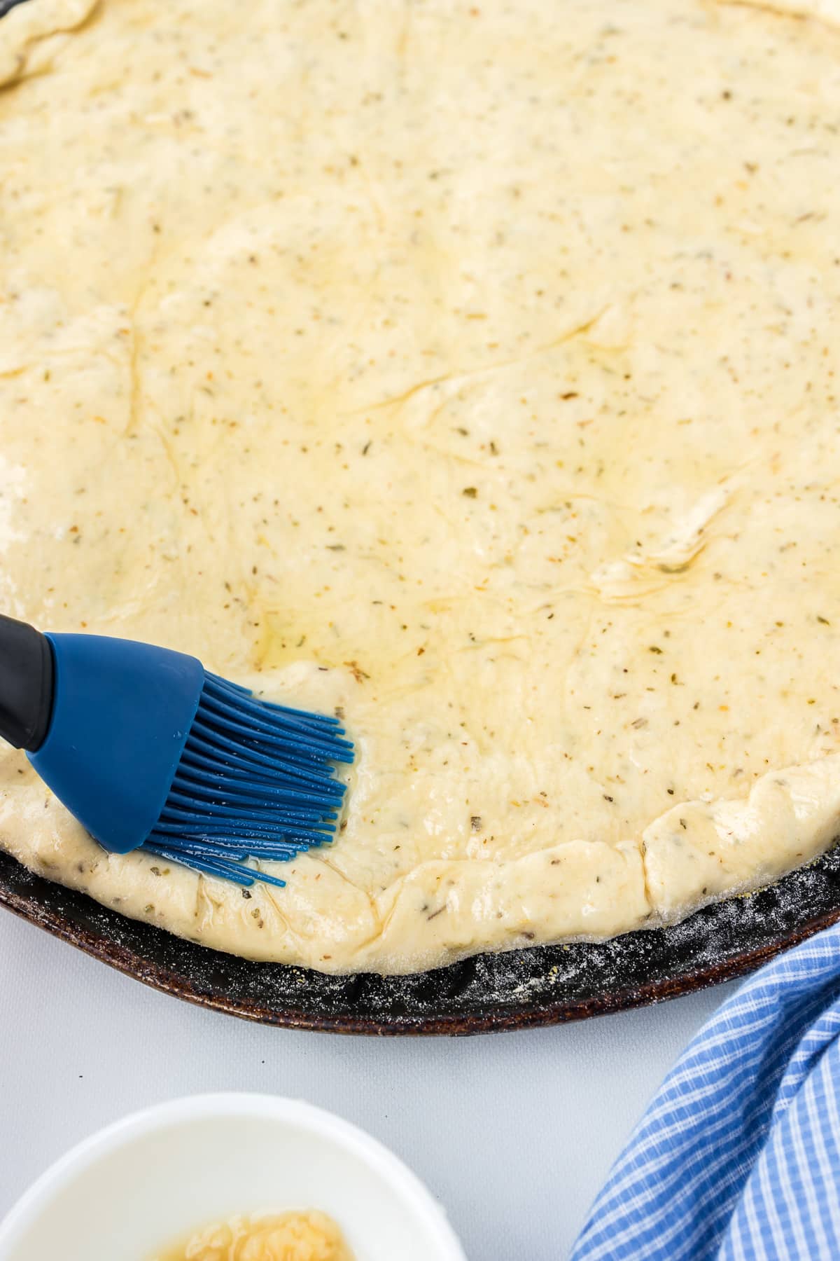 Pizza dough close up being brushed with oil with a silicone brush.