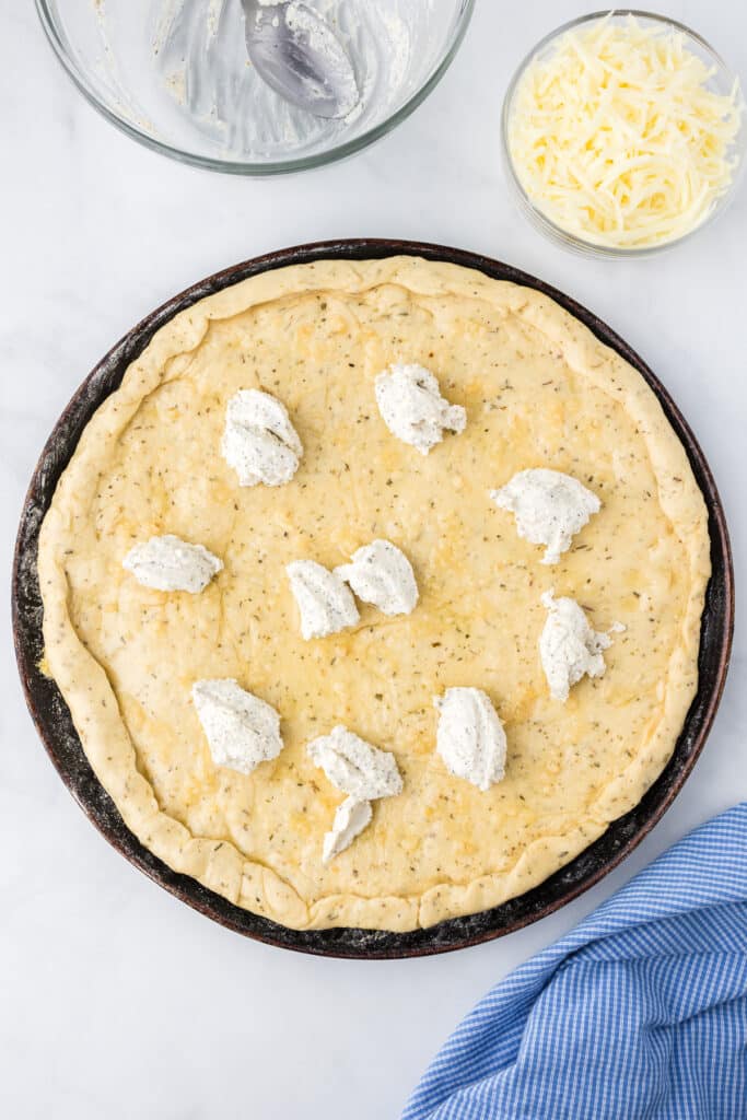 Ricotta mixture dolloped on the pizza crust.