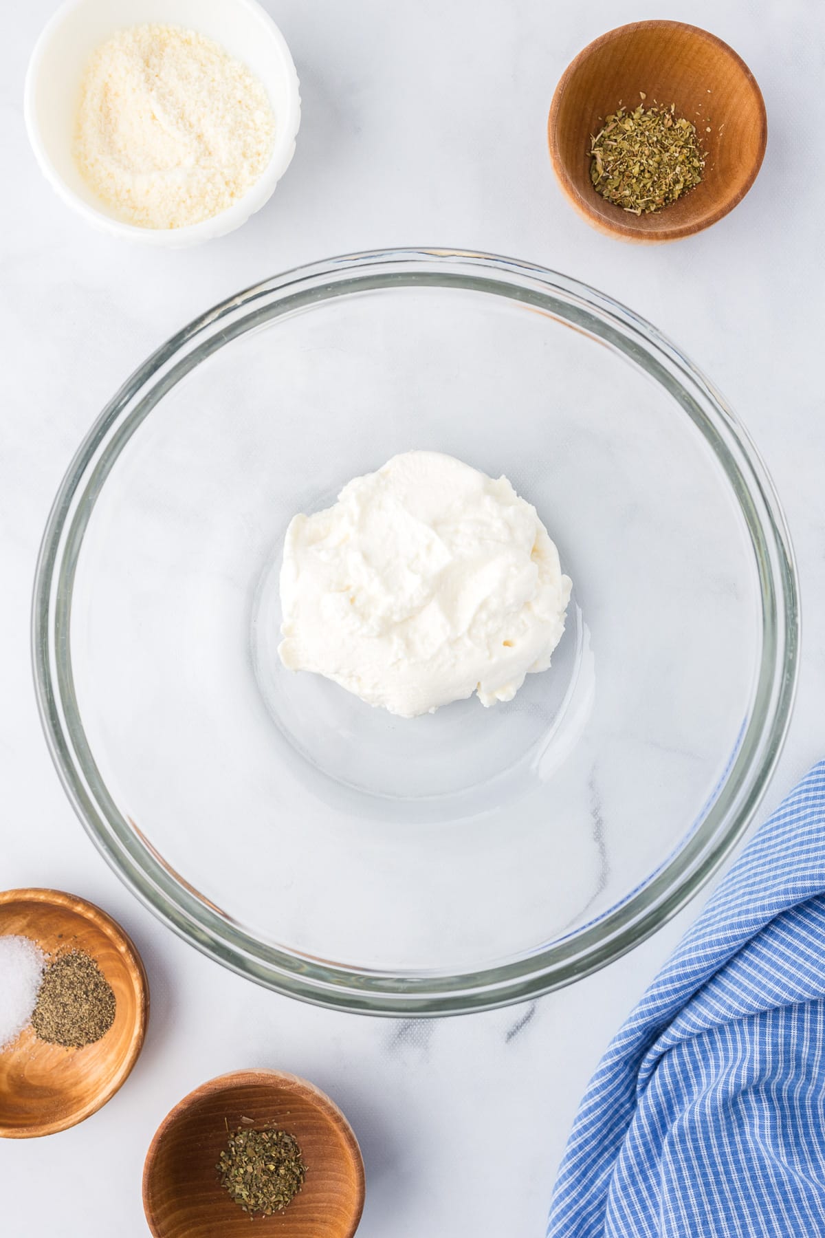 Ricotta in a large mixing bowl from above on a counter with parmesan cheese and other spices in bowls nearby.
