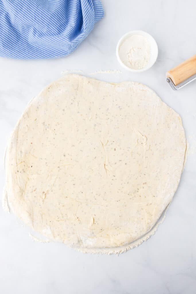 Pizza dough being stretched on a counter covered lightly in flour.