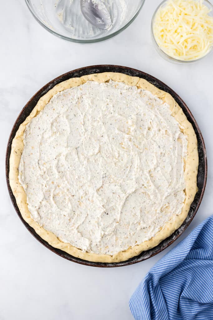 Herbed ricotta mixture spread over pizza crust on a pan from overhead.