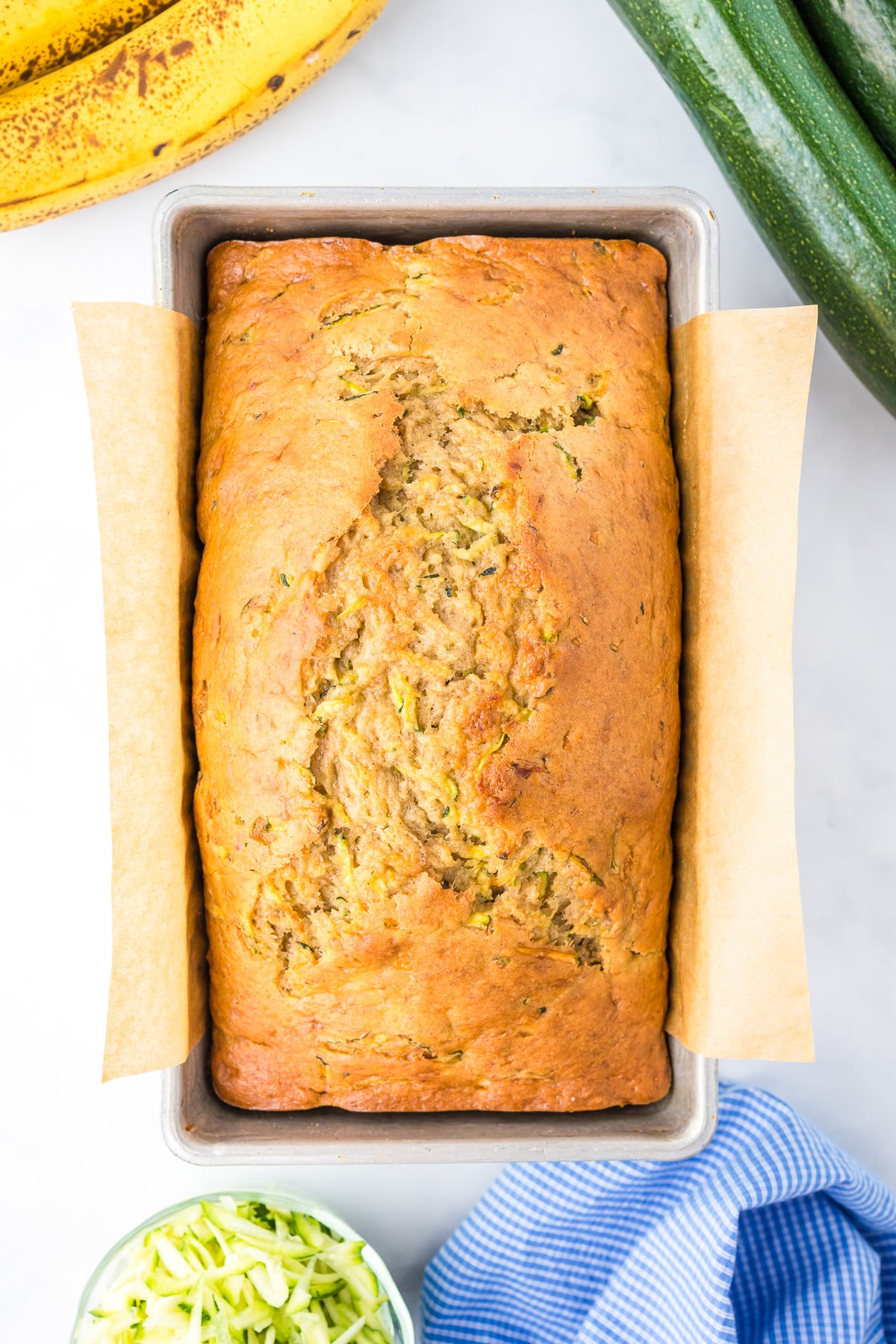 Baked zucchini banana bread in a parchment lined bread pan from overhead on a counter.
