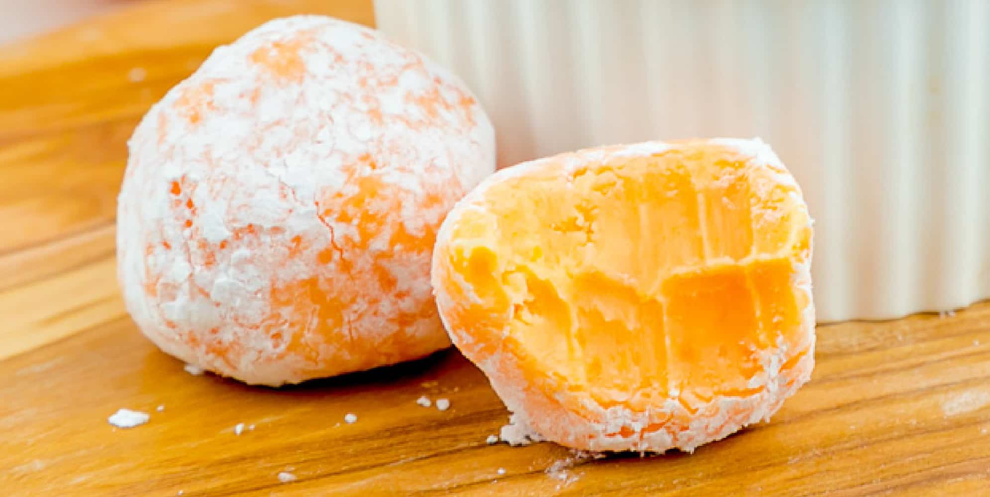 Wide view of two orange creamsicle truffles covered in powdered sugar with one missing a bite.