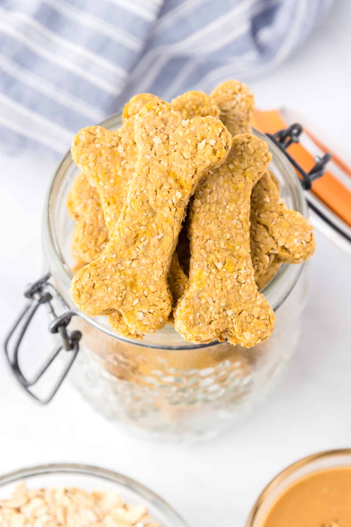 Peanut butter cookies for dogs in the shape of dog bones piled in a large glass jar on a counter.