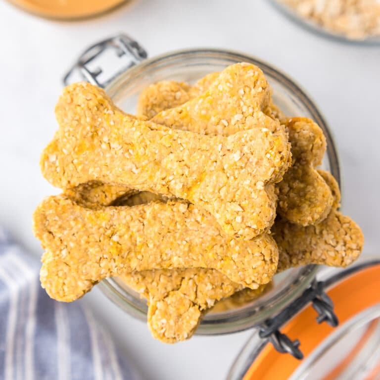 Square view of peanut butter dog bone shaped cookies in a glass jar open from overhead.